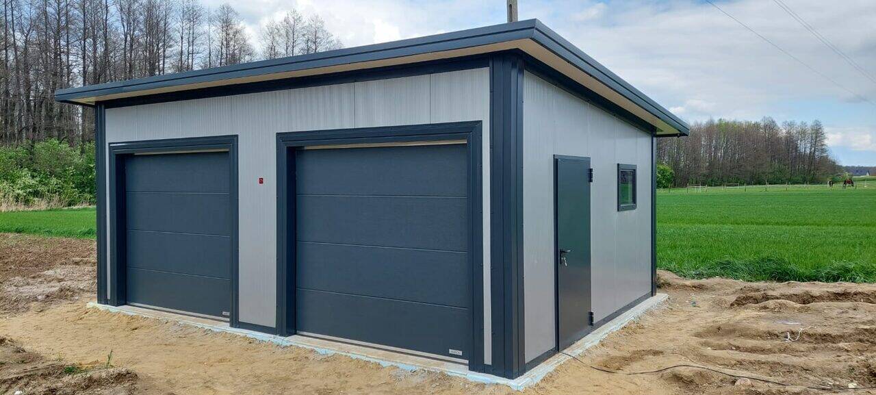 Grey insulated PIR double garage with two anthracite sectional doors, front three-quarter view beside open fields