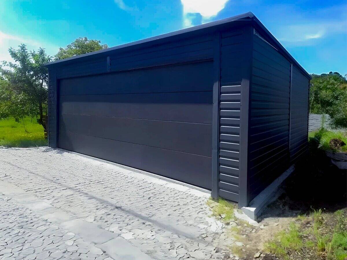 Graphite steel garage with rear-pitch roof, front-left view in garden setting with trees