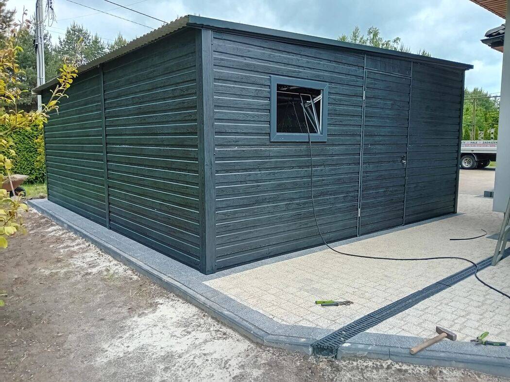 Anthracite steel garage with side door visible, front three-quarter view on concrete driveway