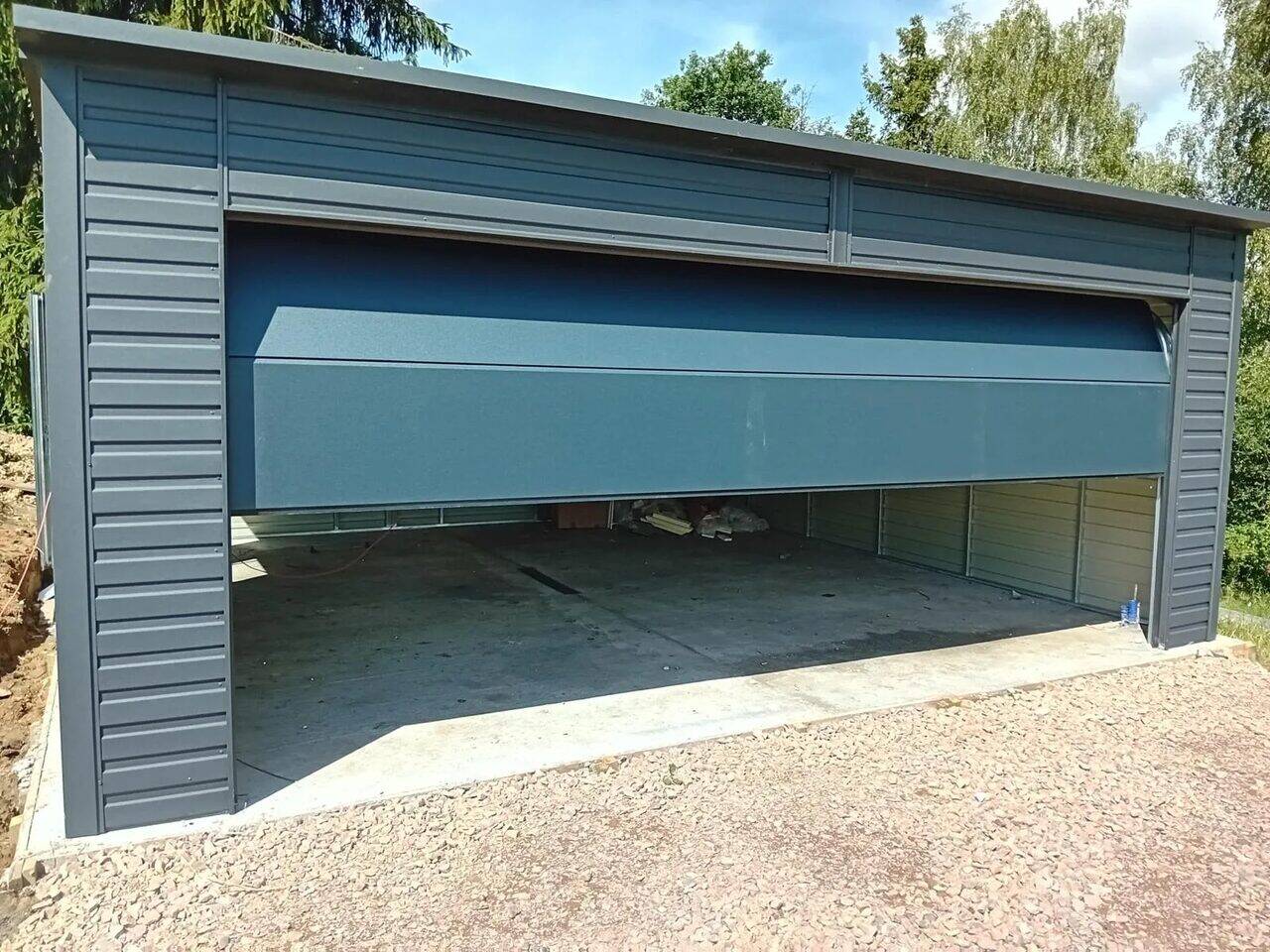 Anthracite steel garage with the sectional door fully open, front three-quarter view on gravel