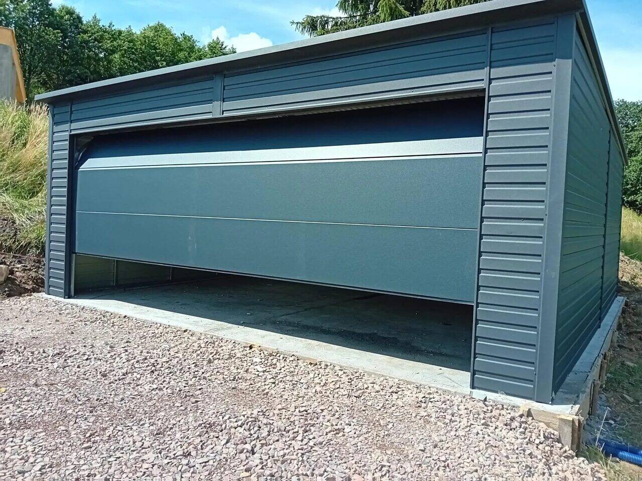 Anthracite steel garage with the sectional door open, front-left three-quarter view on a gravel driveway